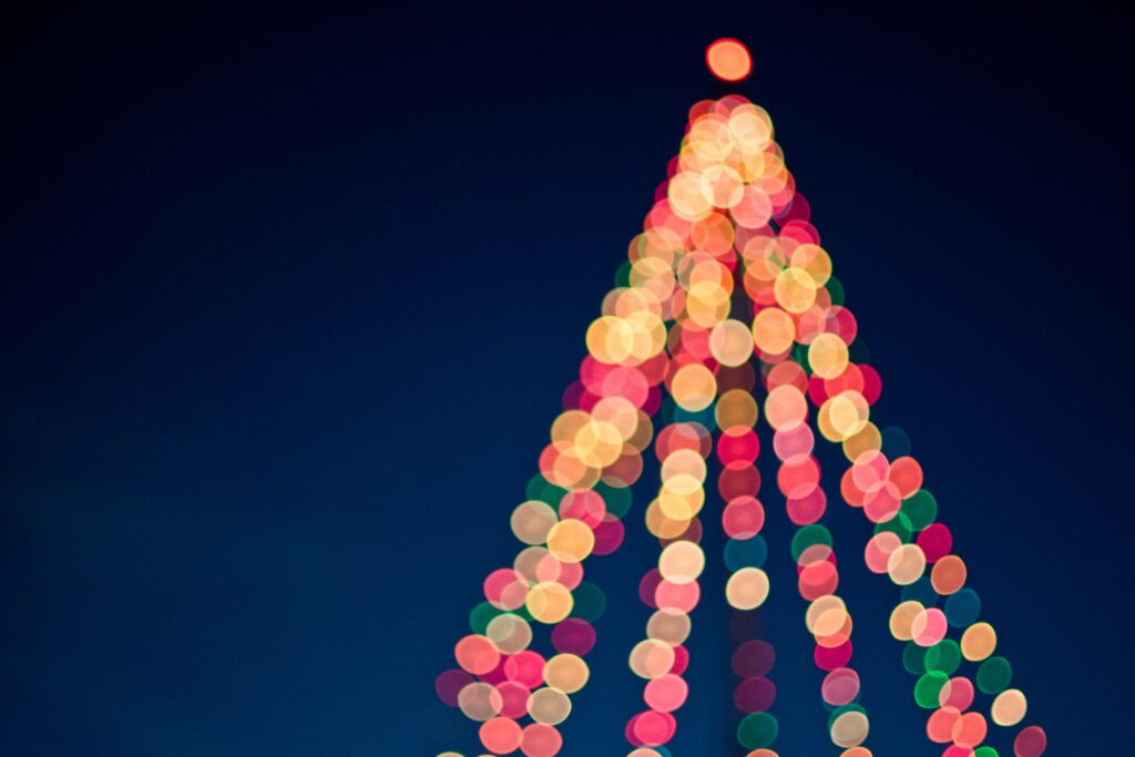 Colorful bokeh lights forming a Christmas tree against a dark blue sky.