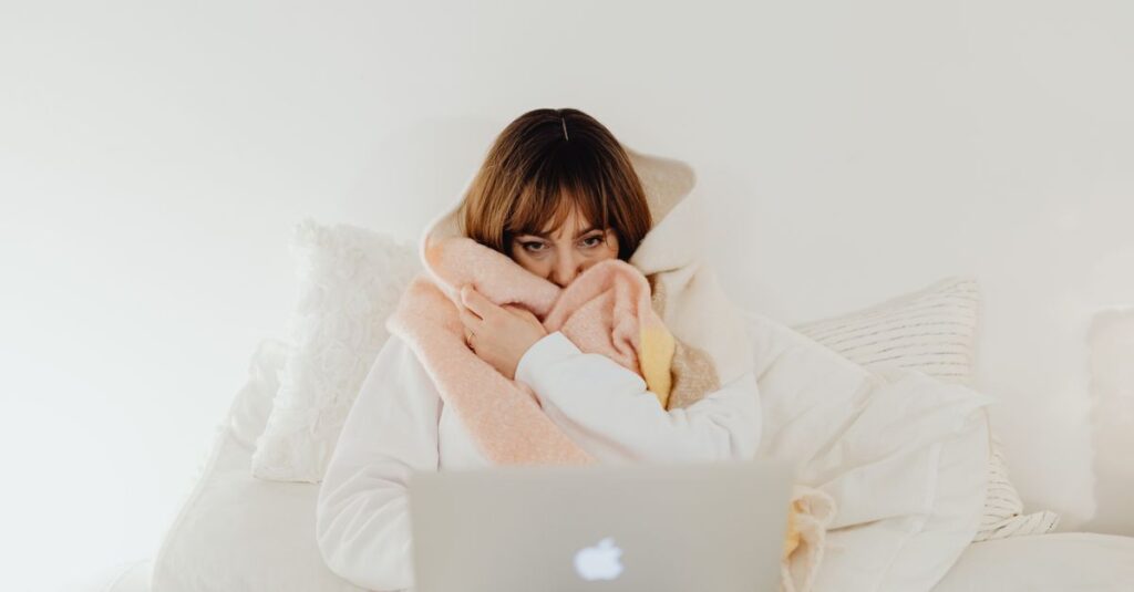 Woman wrapped in a warm blanket using a laptop on a cozy bed. Perfect for representing comfort and leisure at home.