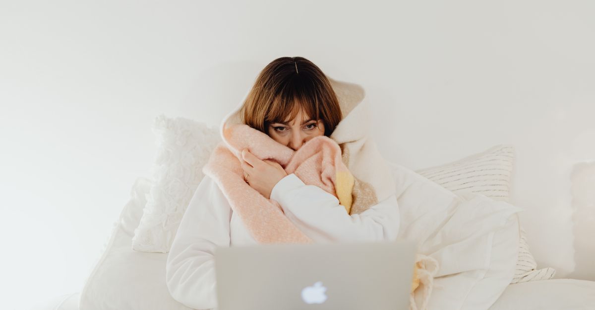 Woman wrapped in a warm blanket using a laptop on a cozy bed. Perfect for representing comfort and leisure at home.