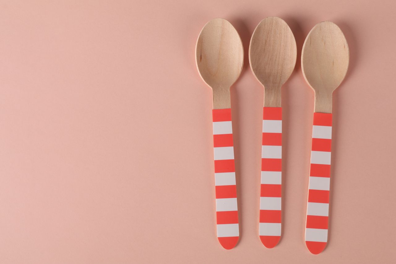 Three eco-friendly wooden spoons with striped handles on a minimalist pink background.